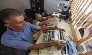 Men count wads of Iraqi dinars using money counting machines at a currency exchange shop in Baghdad
