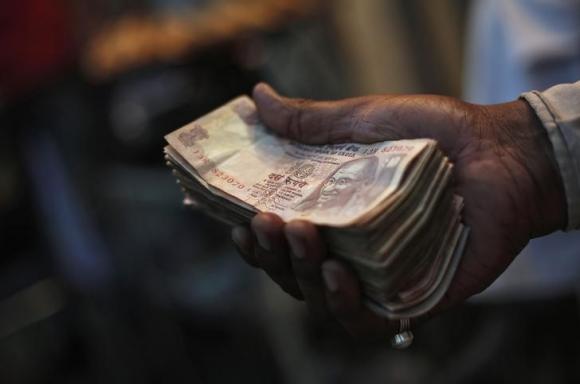 A street side restaurant owner holds a bundle of Indian currency notes as he sits outside his restaurant in New Delhi