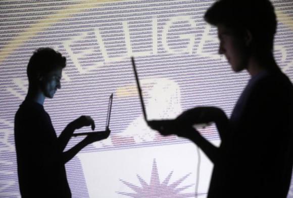 People pose with laptops in front of projection of binary code and CIA emblem in this picture illustration taken in Zenica