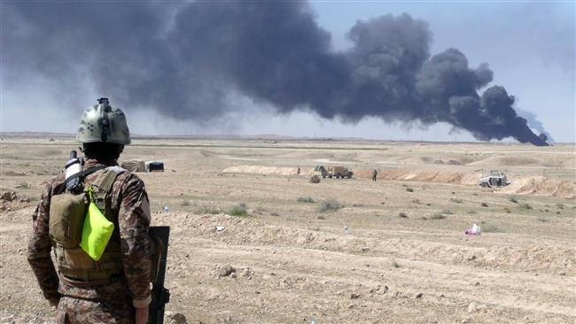 An Iraqi soldier stands looking at smoke billowing from the Ajeel oil field located 35km (22 miles) northeast of Tikrit on March 11, 2015.